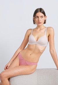 Gaiši rozā bezšuvju krūšturis ar regulējamām lencēm un smalku polsterējumu; komplektā ar caurspīdīgām rozā bikini biksītēm ar mežģīņu akcentiem.