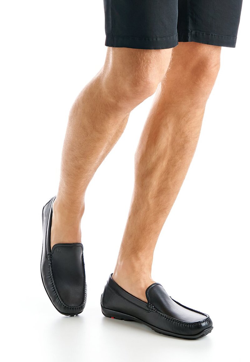 Zwarte leren instapschoenen met stikdetails, een ronde neus en een getextureerde zool, gedragen met zwarte shorts, die een casual stijl laten zien.