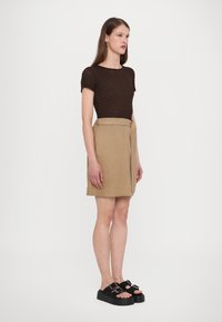 Brown knit top paired with a beige fold-over skirt. Model wears black platform sandals with dual buckles. Simple, modern design.