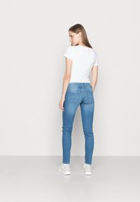 Jeans skinny azul claro com uma cintura média, bolsos traseiros moldados e uma textura de denim suave, acompanhados de uma t-shirt branca justa.