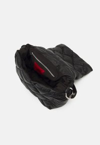 Svart vadderad läderväska med mjuk textur, med en dragkedjeficka inuti och en kontrasterande röd foder. Stor, oval form med en silverring.