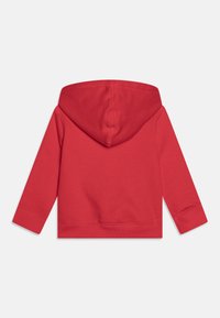 Punainen huppari, jossa on pitkähihaiset hihat ja ribbireunat. Pehmeä rakenne ilman saumoja, jossa on yksivärinen muotoilu ilman kuvioita.