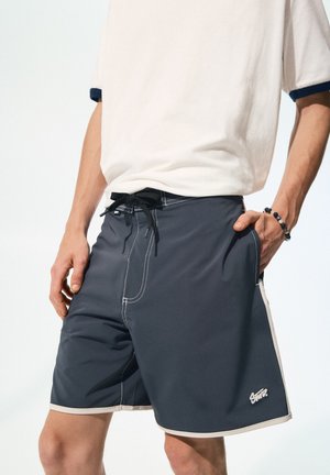 Graue Schwimmshorts mit kontrastierendem weißen Nähten und einem schwarzen Kordelzug. Verfügt über zwei Seitentaschen und ein kleines Logo am Saum.