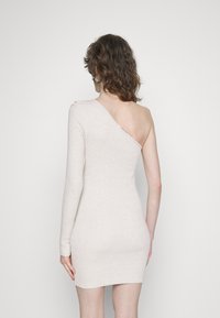 Vestido de malha de mangas compridas em bege claro com um design assimétrico. Um ombro está descoberto, apresentando uma silhueta ajustada e uma textura suave.