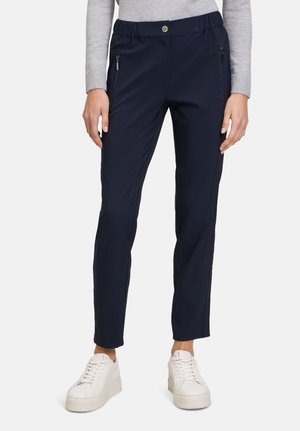 Pantaloni elasticizzati blu navy con vestibilità comoda, vita elasticizzata, tasche laterali con zip e dettagli di cucitura sottili, abbinati a sneakers bianche.