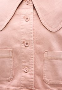 Φωτεινό ροζ τζιν μπουφάν με στρογγυλή γιακά, κλείσιμο με πέντε κουμπιά και δύο μπροστινές τσέπες με διακριτικές λεπτομέρειες ραφής.