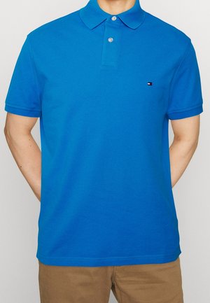 Polo bleu à manches courtes avec un col à revers, doté d'une patte de boutonnage à trois boutons et d'un petit logo sur la poitrine gauche.