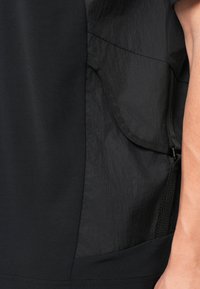 Μαύρο ρούχο με υφασμάτινη επιφάνεια, που διαθέτει λεία υφή από τη μια πλευρά και ρυτιδωμένη φινέτσα από την άλλη, συμπληρωμένο με ρυθμιζόμενες λεπτομέρειες.