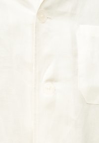 Gros plan sur un tissu blanc avec deux boutons ronds et une petite poche sur le côté droit.