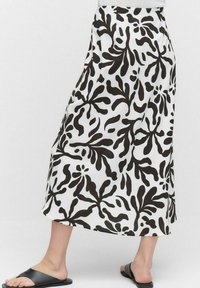 Jupe maxi avec un motif de feuilles noires audacieux sur un fond blanc. Fabriquée en tissu léger avec une taille élastique. Design simple et fluide.