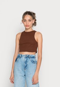 Top cropped castanho com textura canelada e decote alto, combinado com jeans de ganga azuis claros de cintura alta com bolsos frontais.