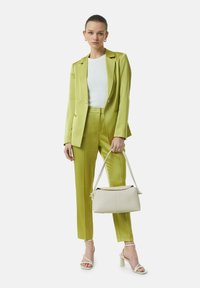Zielona satynowa garsonka z usztywnianą marynarką i dopasowanymi spodniami, połączona z białym topem ze żłobieniami, białą torebką i białymi sandałami na obcasie.