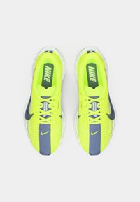 Neon yellow running shoes with grey accents, mesh upper, padded tongue, and visible cushioning on a transparent sole. Nike logo on each shoe.