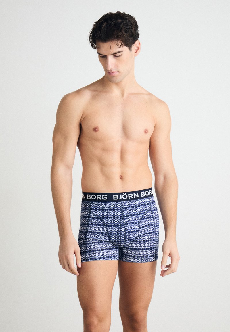 Črne in bele boxer hlače z vzorcem in črnim pasom, na katerem je logo "BJÖRN BORG". Narejene so iz mehkega materiala, s prilegnjeno zasnovo in brez vidnih šivov.