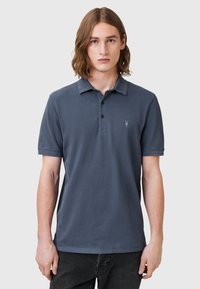 Marinblå pikétröja i bomull, kort ärm, treknappslåning, broderad logotyp på vänster bröst och klassisk kragsdesign.