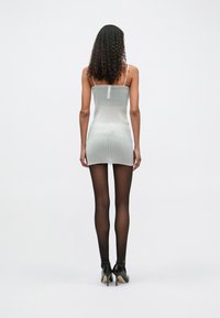 Ασημένιο μίνι φόρεμα με ριγέ σχέδιο, λεπτές τιράντες, εφαρμοστό σχήμα και μήκος πάνω από το γόνατο, συνδυασμένο με μαύρες διάφανες κολάν και ψηλές γόβες.