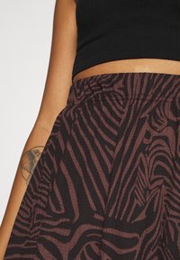 Gonna con cintura elasticizzata in un tessuto marrone scuro testurizzato, caratterizzata da un motivo a zebra in tonalità più chiare.