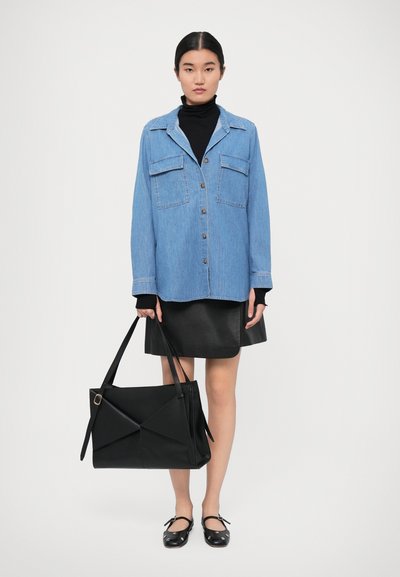 Camicia di jeans con chiusura a bottoni, due tasche sul petto; abbinata a una gonna di pelle nera e a una borsa a tracolla nera strutturata. Il modello indossa delle ballerine nere.