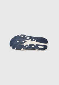 Navy athletic shoe sole with textured rubber, featuring a unique pattern of cutouts and grooves for traction, and a cream-colored border.