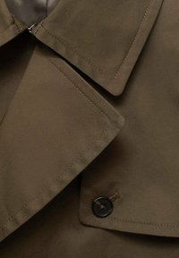 Bruine trenchcoat met een grote kraag, knoopsluiting en een gladde, textuurgeweven stof met zichtbare stiksels.