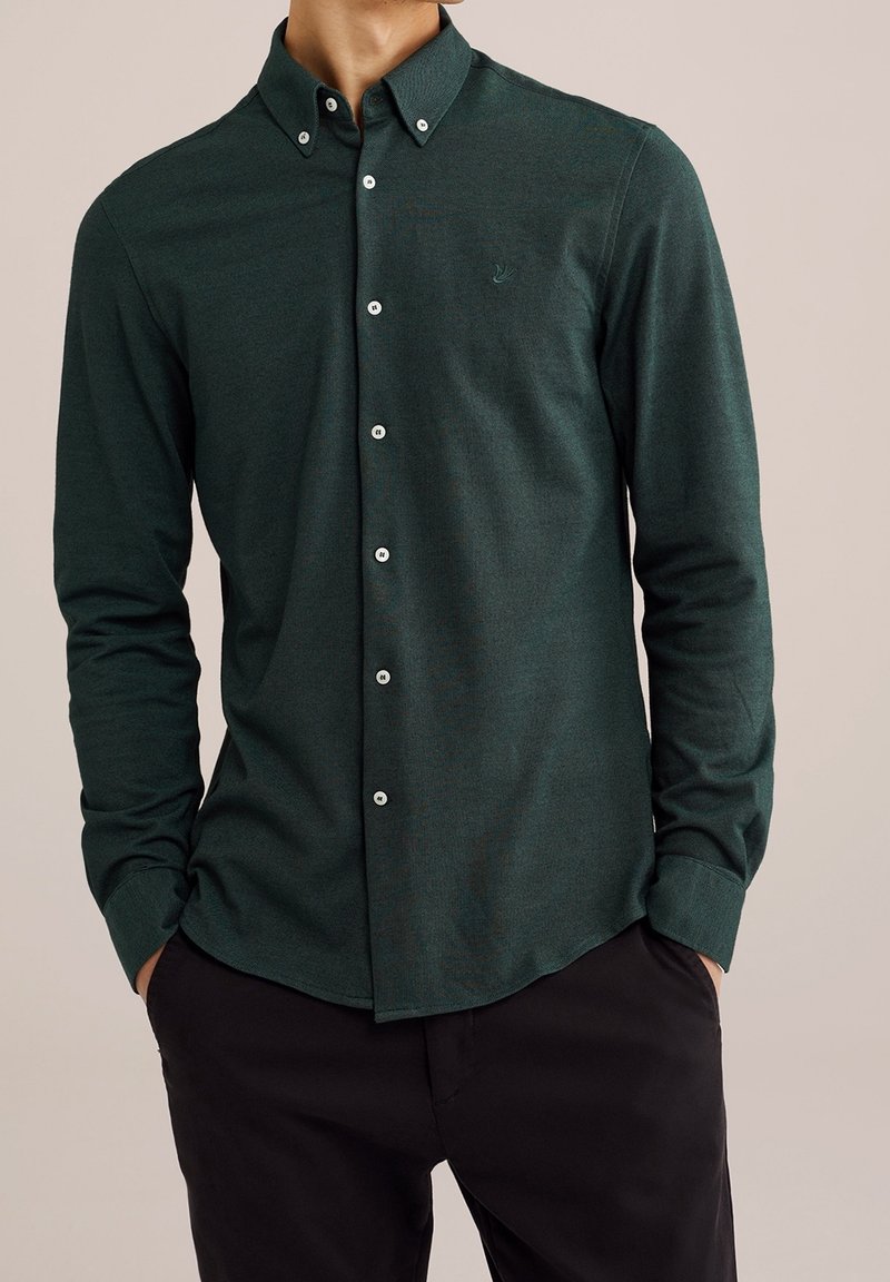 Mörkgrön skjorta med knappar framtill och långa ärmar, med en knapp-ner krage och en subtil logotyp. Tillverkad av textil med struktur och knappar fram.