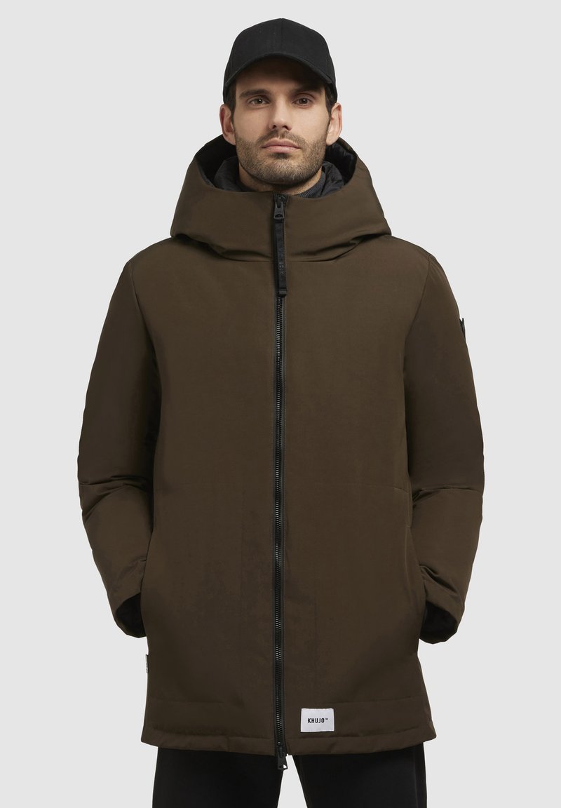 Brun isoleret parka med høj krave og hætte, der har en lynlås foran og to lommer, lavet af glat, vandafvisende materiale.