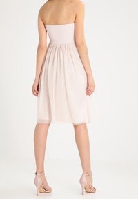 Bezramienna, jasno różowa sukienka z marszczonym topem i zwiewnym, półprzezroczystym dołem. Połączona z cielistymi, wysokimi sandałami.