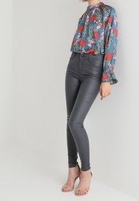Blusa de estampado floral con puños acampanados en tonos azul y rojo, combinada con pantalones ajustados de imitación piel gris y tacones de color rosa claro.