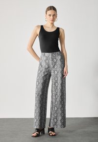 Zwarte mouwloze top gecombineerd met wijde broek met een grijs-wit slangenhuidpatroon. De broek heeft een hoge taille en voorzakken.