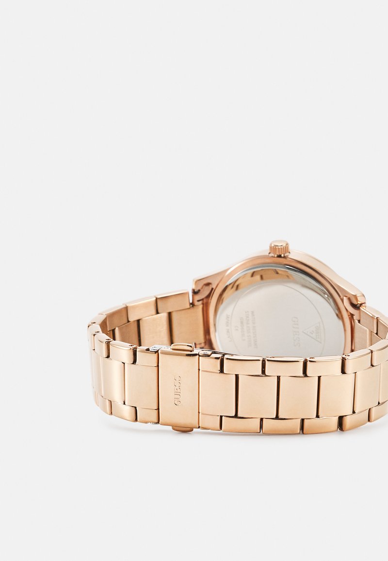 Roségoldene Metall-Uhr mit einem Gliederarmband, rundem Gehäuse und sichtbarem Rückdeckel. Verfügt über ein Logo und eine detaillierte Gravur auf der Schließe.