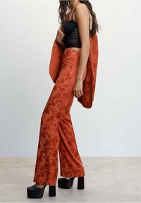 Punaiset teksturoidut housut kukkakuviolla, yhdistettynä mustaan vartalonmyötäiseen toppiin ja korokepohjaisiin korkokenkiin. Kangas näyttää sileältä ja laskeutuu kauniisti.