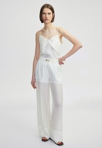 Leichter weißer Jumpsuit mit einem geschichteten Oberteil und weit geschnittenen, transparenten Hosen mit elastischem Bund und Schleifendetail. Glatte Textur.
