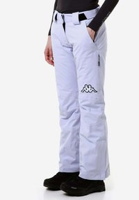 I pantaloni da neve viola chiaro presentano una cintura, tasche laterali e una tasca con zip. C'è un dettaglio del logo nero sulla coscia sinistra.