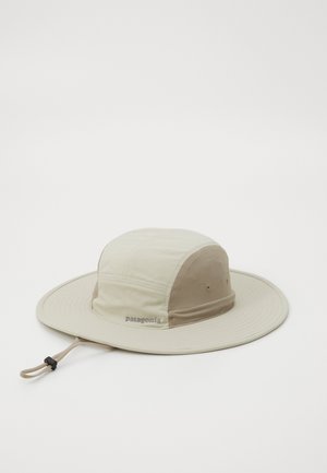 Sombrero de ala ancha beige con una corona estructurada, que presenta una tela texturizada y un cordón con un regulador ajustable. Logo de "Patagonia" visible.