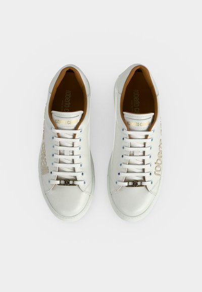 Paire de baskets basses en cuir blanc avec lacets blancs, logo en lettres dorées sur les côtés et les languettes, et doublure intérieure marron.