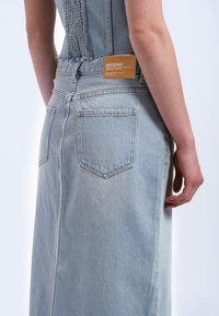 Ljusblå denimkjol med en figursydd midja, två bakfickor och en märkesetikett. Tyget har en lätt textur och en rå sömdetalj.