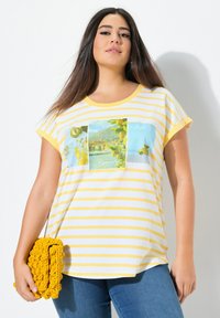 Keltainen ja valkoinen raidallinen lyhythihainen t-paita, jossa on kolme graafista paneelia. Pehmeä kangas, rento malli, yhdistettynä teksturoituun keltaiseen clutch-laukkuun.