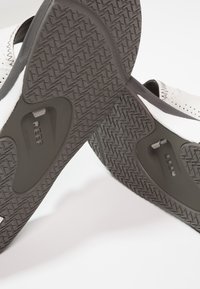 Sandales noir et blanc avec semelles en caoutchouc texturé, présentant un dessus en cuir perforé et un matériel ajustable sur les côtés.