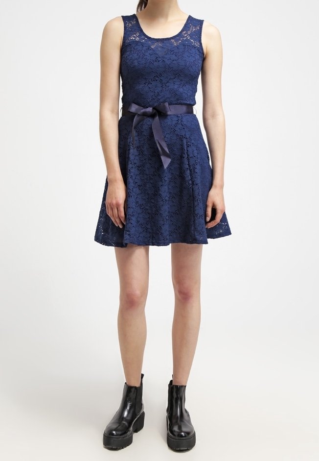 Robe en dentelle bleu marine avec un corsage ajusté, une jupe évasée et un nœud en ruban à la taille. Associée à des bottines noires à semelles épaisses.