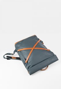 Zaino in pelle grigia con spallacci arancioni, design a risvolto e finitura testurizzata. Include una maniglia superiore e spallacci regolabili.