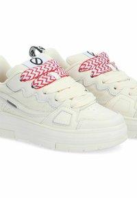 Des baskets blanches massives en matériaux lisses et texturés, avec des lacets à motifs chevrons rouge et blanc et une étiquette de logo sur la languette.