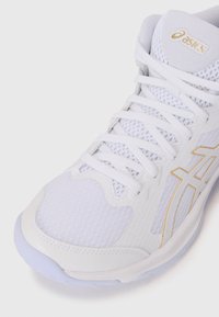 White athletic shoe with mesh and synthetic upper, white laces, gold brand logo, textured detailing, and a light gray outsole.