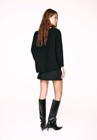 Czarny dzianinowy sweter, krótka czarna spódnica i czarne skórzane kozaki za kolano. Gładka faktura, dopasowana sylwetka i szczegół z ostrym noskiem.