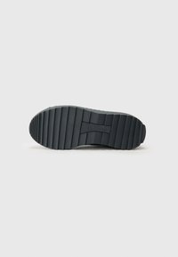 Semelle de chaussure en caoutchouc noir avec des rainures texturées et horizontales, et un bout arrondi. Logo visible sur le côté, mettant en avant la fonctionnalité et l'adhérence.