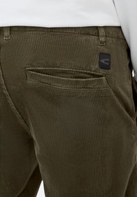 Olive green corduroy pants with a ribbed texture, featuring a back pocket and a small black logo patch.