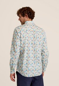 Langarmshirt met een meerkleurig bladerenpatroon op een lichte achtergrond. Voorzien van een button-down kraag en verstelbare manchetten.
