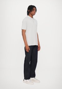 Světle šedá polo košile s límečkem, kombinovaná s tmavými denimovými džíny. Bílé tenisky dokončují outfit. Jednoduchý, casual design bez vzorů.