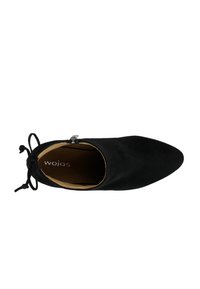 Scarpa in suede nera con punta affusolata, dettaglio di laccio decorativo e zip laterale. L'interno presenta una fodera chiara con il nome del marchio "wojas."