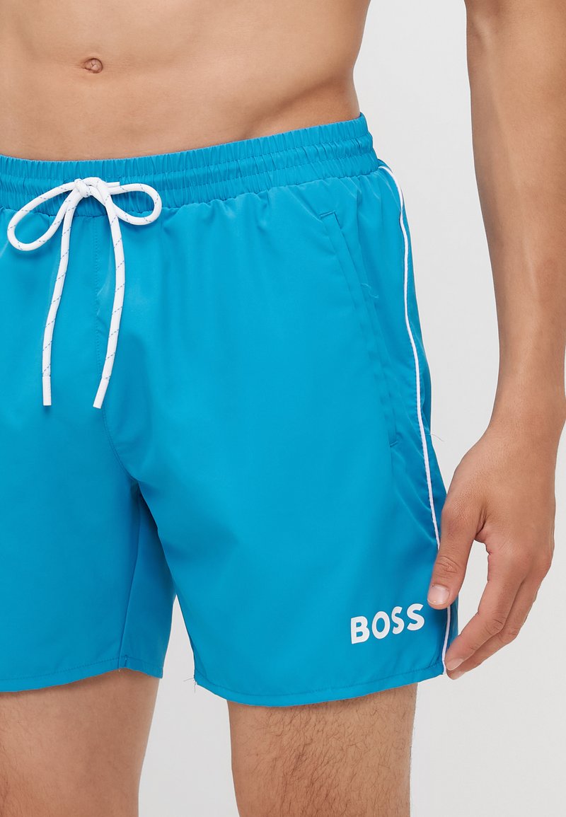 Turquoise zwemboxers met een elastische tailleband, witte trekkoord en wit logo op het linkerbeen. Gladde, lichte stof.