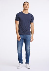 Granatowa bawełniana koszulka z okrągłym dekoltem, dopasowany krój, w połączeniu z jasnoniebieskimi dżinsami i białymi trampkami, minimalne detale.
